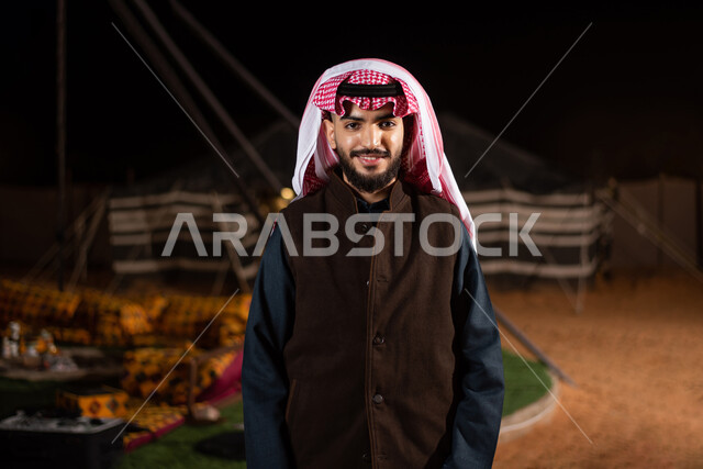 A Saudi Arabian Gulf man wearing a winter jacket, warm winter clothes, a wild camping trip in the desert, tourist camps in the desert, popular tents in the deserts of Saudi Arabia, an evening youth camp, a winter night atmosphere