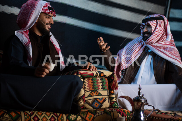 رجلان خليجيان سعوديان عربيان يستمتعان برحلة تخييم برية في صحراء السعودية، شرب القهوة العربية، حوارات ونقاشات بين الاصدقاء، دلة قهوة، جلسة بر عربية شعبية، كشتة بر شبابية مسائية، مخيمات سياحية في الصحراء، اجواء شتوية ليلية