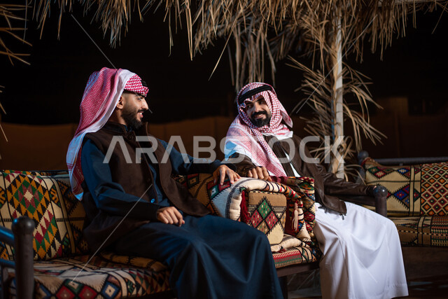 رجلان عربيان خليجيان سعوديان يقضيان اوقات ممتعة في صحراء السعودية، ارتداء ملابس الشتاء الدافئة، رحلة تخييم برية، حوارات ونقاشات بين الاصدقاء، جلسة بر عربية شعبية، كشتة بر شبابية مسائية، مخيمات سياحية في الصحراء، اجواء شتوية ليلية