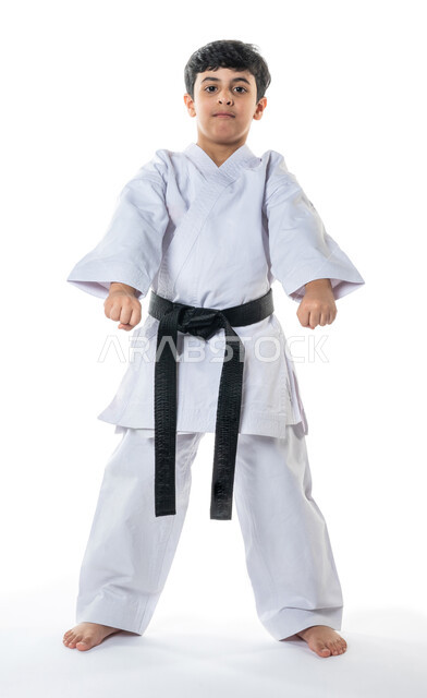 Portrait of a Saudi Arabian Gulf child practicing karate, martial movements, white karate uniform with black belt, taekwondo, recreational sports activities for children, full-length body image, white background.