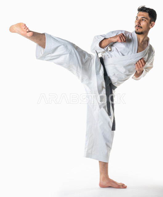  التدرب على حركات قتالية خاصة, بورتريه لرجل عربي خليجي سعودي يمارس رياضة الكاراتيه اليابانية، تطبيق حركات الكاتا, زي الكاراتيه الأبيض مع الحزام الأسود، فنون الدفاع عن النفس، فنون قتالية يابانية، القوة البدنية، صورة الجسم بالطول الكامل, خلفية بيضاء.