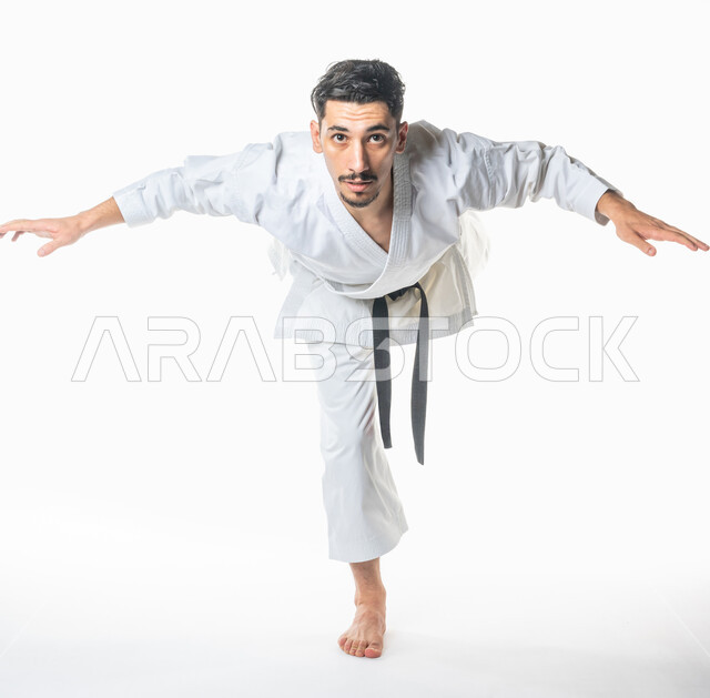 بورتريه امامي لرجل عربي خليجي سعودي يمارس رياضة الكاراتيه اليابانية، رياضة التايكواندو, زي الكاراتيه الأبيض مع الحزام الأسود، التدرب على حركات قتالية خاصة، فنون الدفاع عن النفس، بطولات رياضة الكاراتيه، صورة الجسم بالطول الكامل, خلفية بيضاء