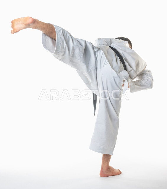 تطبيق حركات الكاتا, بورتريه من الخلف لرجل عربي خليجي سعودي يمارس رياضة الكاراتيه اليابانية, زي الكاراتيه الأبيض مع الحزام الأسود، فنون الدفاع عن النفس، التدرب على حركات قتالية خاصة، فنون قتالية يابانية، صورة الجسم بالطول الكامل, خلفية بيضاء