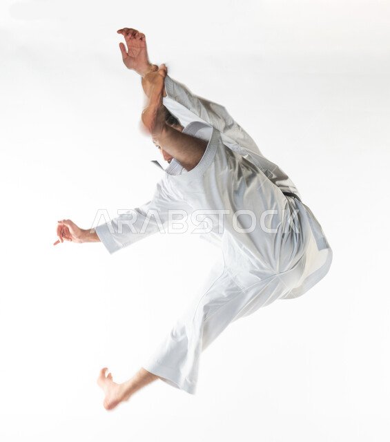 ممارسة رياضة الكاراتيه, بورتريه  لرجل عربي خليجي سعودي يمارس رياضة الكاراتيه اليابانية، زي الكاراتيه الأبيض مع الحزام الأسود، فنون الدفاع عن النفس، التدرب على حركات قتالية خاصة، فنون قتالية يابانية، القوة البدنية، القفز في الهواء, خلفية بيضاء .