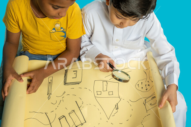 صورة مقربة لطفلان عربيان خليجيان سعوديان يستخدمان العدسة المكبرة، صديقان يفحصان خريطة ورقية، مفهوم الفحص والإستكشاف، الرؤية عن قرب، التحقق والتدقيق، تكبير الاشياء، أدوات بصرية، خلفية زرقاء