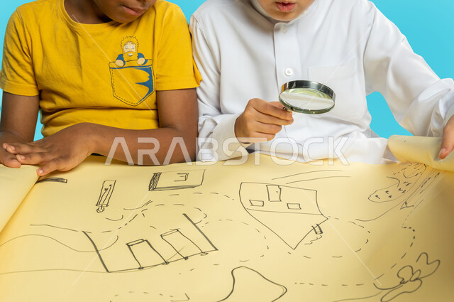 صورة مقربة لطفلان عربيان خليجيان سعوديان يقومان بفحص خريطة ورقية من خلال العدسة المكبرة، مفهوم الفحص والإستكشاف، الرؤية عن قرب، التحقق والتدقيق، تكبير الاشياء، أدوات بصرية، خلفية زرقاء