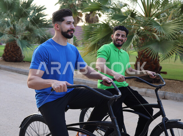 صديقان عربيان خليجيان سعوديان يقودان الدراجه الهوائيه في احد الحدائق العامة، ممارسة هواية ركوب الدراجات، أنشطة ترفيهيه، عطلة صيفية، أماكن عامة, ركوب الدراجات في الهواء الطلق