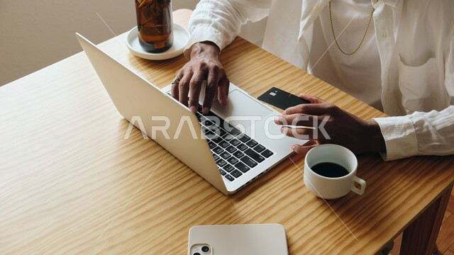 صورة مقربة لرجل عربي خليجي يستخدم جهاز الحاسوب المحمول، جلسة تسوق ،  استخدام بطاقة الإئتمان البنكية ، التسوق الالكتروني، الشراء والدفع عبر الحاسوب، إستخدام أجهزة تقنية حديثة ، الدفع الإلكتروني عبر الانترنت ، مهن وأعمال عن بعد، بطاقة الائتمان البنكية، شراء