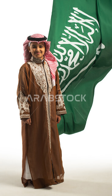 بورتريه لولد عربي خليجي سعودي، خلفية علم السعودية، يرتدي الزي السعودي الشعبي التقليدي، الإحتفالات الوطنية في المنطقة الشمالية، هوية اليوم الوطني السعودي 92،، يوم التأسيس السعودي، زي تراثي سعودي للمناسبات الوطنية، صورة للجسم بالطول الكامل، العيد الوطني