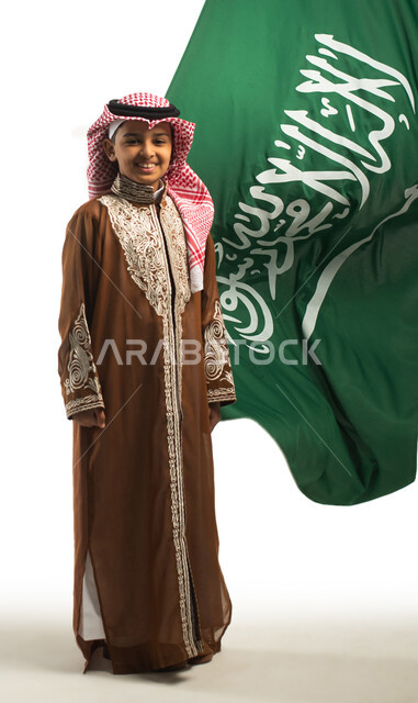 بورتريه لولد عربي خليجي سعودي، خلفية علم السعودية، يرتدي الزي السعودي الشعبي التقليدي، الإحتفالات الوطنية في المنطقة الشمالية، هوية اليوم الوطني السعودي 92،، يوم التأسيس السعودي، زي تراثي سعودي للمناسبات الوطنية، صورة للجسم بالطول الكامل، العيد الوطني