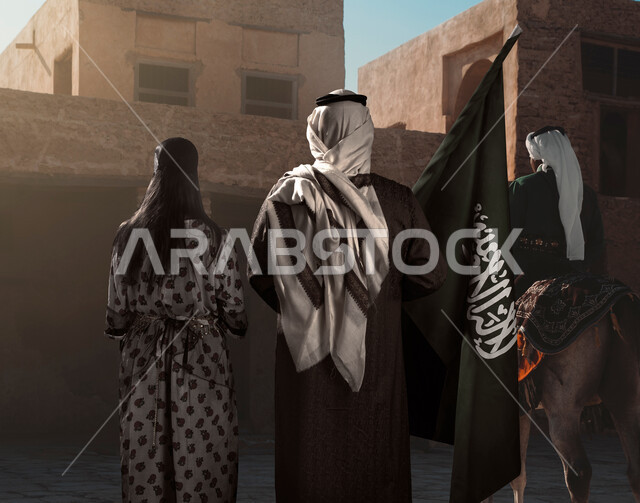 مجموعة من الأشخاص العربيون السعوديون الخليجيون يرتدون الزي السعودي الشعبي التقليدي ، أزياء المناسبات والإحتفالات الوطنيه, زي يوم التأسيس السعودي, اليوم الوطني السعودي , ذكرى يوم تأسيس المملكة العربية السعودية 1727 , خلفية البيوت الأثرية في السعودية