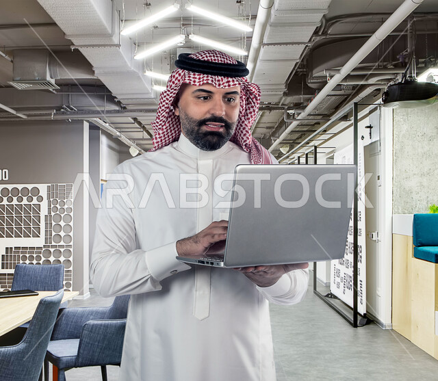 رجل عربي خليجي سعودي يستخدم جهاز الحاسوب المحمول لتطوير شبكة الحاسوب والانظمة البرمجية ، العمل عن بعد ، تكنولوجيا المعلومات ، خلفية هولوجرام ثلاثية الابعاد