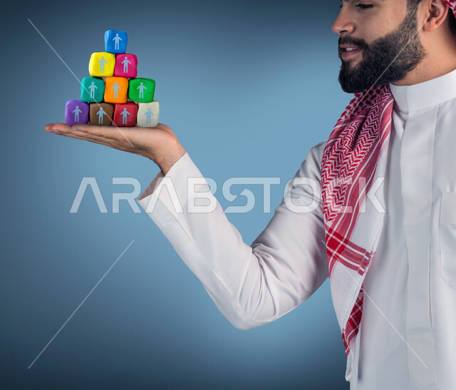 صورة مقربة لرجل عربي خليجي سعودي يحمل بيده مجموعة من المكعبات، رموز واشكال، مكعبات ملونة، ايماءات وجه ويدين مختلفة، خلفية زرقاء