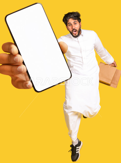Portrait of a Saudi Arabian Gulf man, displaying a large mobile phone screen, white hollow mobile screen, jumping high, online shopping stores, techniques and technology, e-marketing, yellow background
