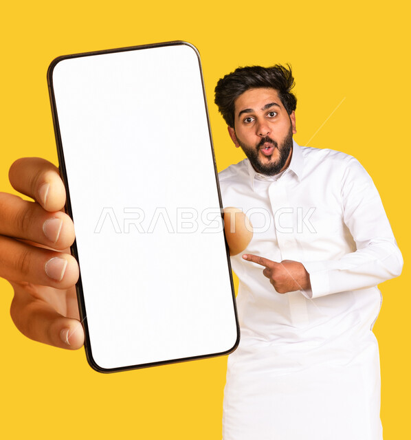 بورتريه رجل عربي خليجي سعودي ، عرض شاشة هاتف محمول كبير الحجم ،شاشة جوال مفرغة باللون الابيض ، قفز عاليا ، متاجر تسوق الكترونية ، تقنيات و تكنولوجيا ، التسويق الإلكتروني ، خلفية صفراء
