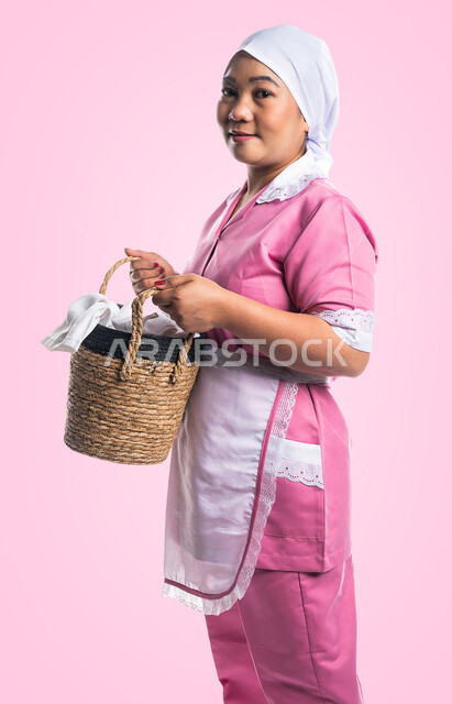 عاملة نظافة تحمل بيدها سلة خاصة بادوات التنظيف المنزلية، النظافة والتطهير، مدبرة منزلية، ادوات ومعدات التنظيف، خادمة منزلية اجنبية، التنظيف وحماية المنزل، خلفية ملونة