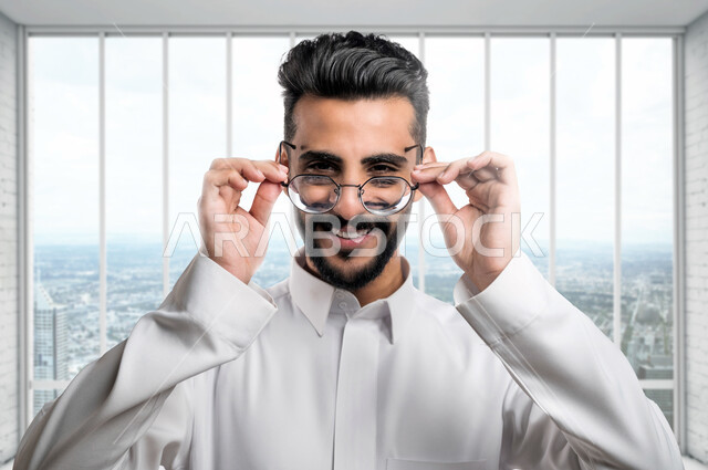 صورة مقربة لرجل عربي خليجي سعودي يرتدي نظارة طبية خاصة بضعف النظر، ايماءات وجه مبتسمة، فحص النظر، قياس النظر، مفهوم ضعف البصر، قصر النظر، الرؤية من خلال النظارة الطبية