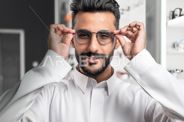 صورة مقربة لرجل عربي خليجي سعودي يرتدي نظارة طبية خاصة بضعف النظر، مفهوم ضعف البصر، قصر النظر، ايماءات وجه مبتسمة، الرؤية من خلال النظارة الطبية