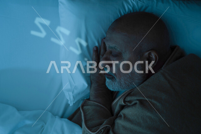 رجل مسن عربي خليجي سعودي يرتدي ملابس الشتاء الدافئة اثناء النوم، ارتداء معطف الشتاء، وسادة بيضاء ناعمة، وقت النوم، النوم المبكر، الاسترخاء والراحة، الاستمتاع بنوم هادئ وصحي