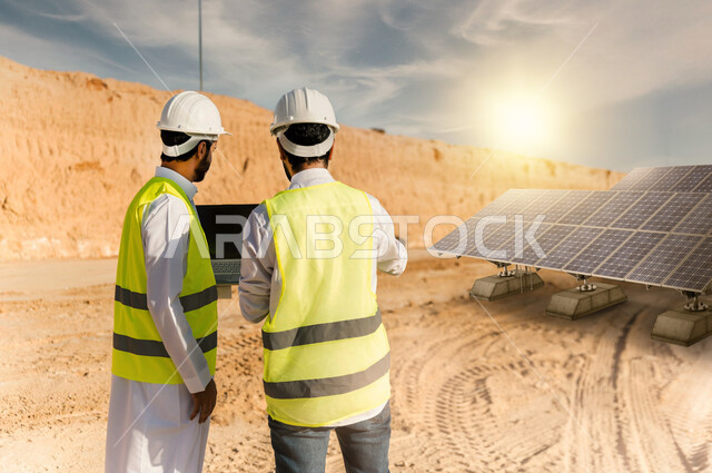 إرتداء خوذة وسترة الحماية ، صورة من الخلف مهندسان عربيان خليجيان سعوديان في الصحراء العربية السعودية , التخطيط والتدقيق و الاشراف على محطات الطاقة الشمسية ، أنظمة الطاقة الشمسية، الطاقة المتجددة،  خلفية الصحراء .