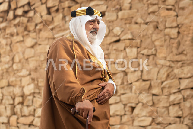 رجل مسن عربي سعودي خليجي يرتدي الزي السعودي الشعبي التقليدي, الزي التراثي للمناسبات الوطنيه, التجول في إحدى المباني الطينيه الشعبيه, بيوت تراثيه قديمه, شعبيات, أحياء أثريه قديمه, جوله بين الأحياء الشعبيه