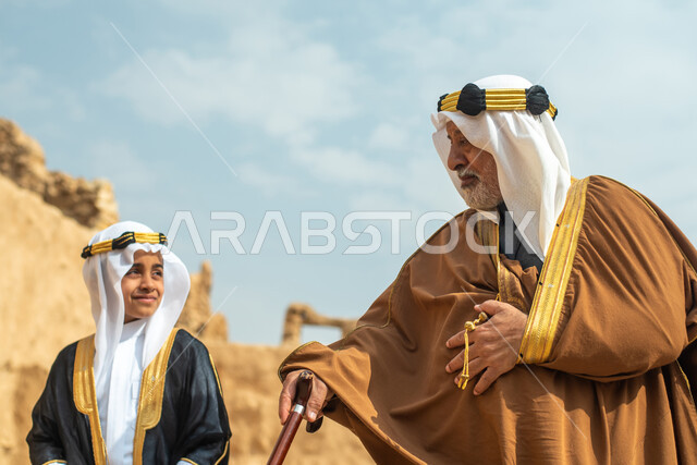An elderly man and a boy, two Saudi Arabs from the Gulf, dressed in the traditional Saudi folk dress, the traditional dress for national occasions, touring in one of the popular mud buildings, old heritage houses, folklore, ancient ancient neighborhoods, 
