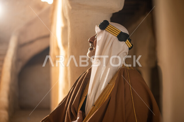 رجل مسن عربي سعودي خليجي يرتدي الزي السعودي الشعبي التقليدي, الزي التراثي للمناسبات الوطنيه, التجول في إحدى المباني الطينيه الشعبيه, بيوت تراثيه قديمه, شعبيات, أحياء أثريه قديمه, جوله بين الأحياء الشعبيه