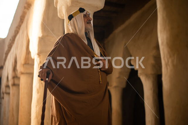 رجل مسن عربي سعودي خليجي يرتدي الزي السعودي الشعبي التقليدي, الزي التراثي للمناسبات الوطنيه, التجول في إحدى المباني الطينيه الشعبيه, بيوت تراثيه قديمه, شعبيات, أحياء أثريه قديمه, جوله بين الأحياء الشعبيه
