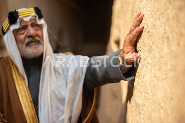 رجل مسن عربي سعودي خليجي يرتدي الزي السعودي الشعبي التقليدي, الزي التراثي للمناسبات الوطنيه, التجول في إحدى المباني الطينيه الشعبيه, بيوت تراثيه قديمه, شعبيات, أحياء أثريه قديمه, جوله بين الأحياء الشعبيه