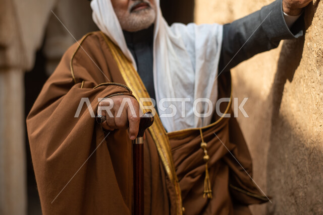 رجل مسن عربي سعودي خليجي يرتدي الزي السعودي الشعبي التقليدي, الزي التراثي للمناسبات الوطنيه, التجول في إحدى المباني الطينيه الشعبيه, بيوت تراثيه قديمه, شعبيات, أحياء أثريه قديمه, جوله بين الأحياء الشعبيه