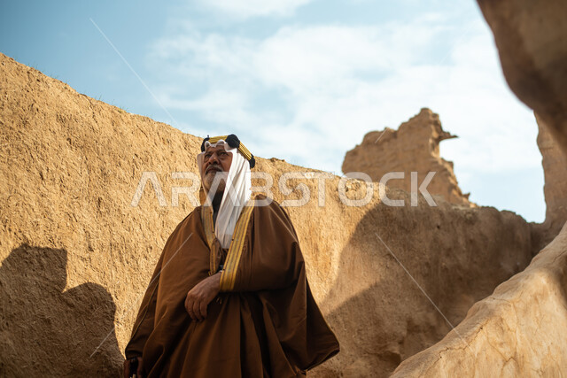 رجل مسن عربي سعودي خليجي يرتدي الزي السعودي الشعبي التقليدي, الزي التراثي للمناسبات الوطنيه, التجول في إحدى المباني الطينيه الشعبيه, بيوت تراثيه قديمه, شعبيات, أحياء أثريه قديمه, جوله بين الأحياء الشعبيه