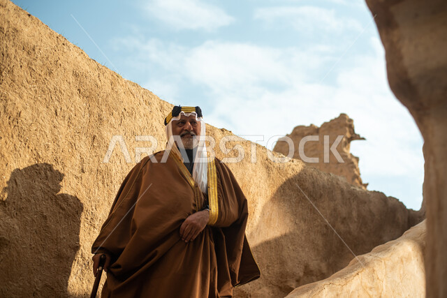 رجل مسن عربي سعودي خليجي يرتدي الزي السعودي الشعبي التقليدي, الزي التراثي للمناسبات الوطنيه, التجول في إحدى المباني الطينيه الشعبيه, بيوت تراثيه قديمه, شعبيات, أحياء أثريه قديمه, جوله بين الأحياء الشعبيه