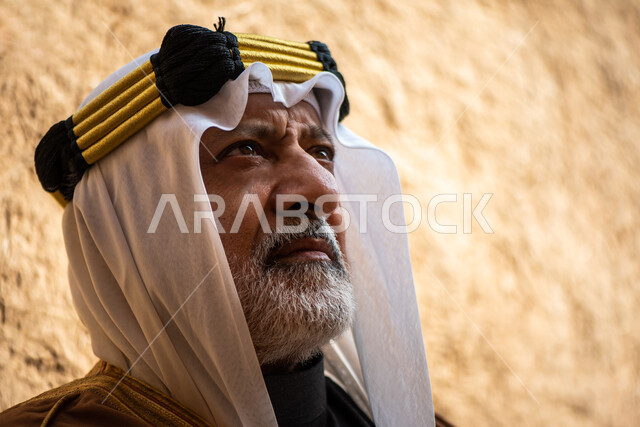 رجل مسن عربي سعودي خليجي يرتدي الزي السعودي الشعبي التقليدي, الزي التراثي للمناسبات الوطنيه, الوقوف في إحدى المباني الطينيه الشعبيه, بيوت تراثيه قديمه, شعبيات, يوم التأسيس السعودي, الإحتفالات الوطنيه في المنطقه الوسطى, مباني أثريه قديمه