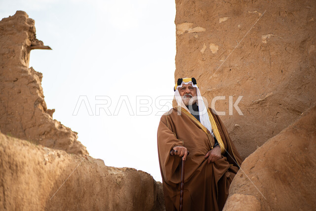 رجل مسن عربي سعودي خليجي يرتدي الزي السعودي الشعبي التقليدي, الزي التراثي للمناسبات الوطنيه, التجول في إحدى المباني الطينيه الشعبيه, بيوت تراثيه قديمه, شعبيات, أحياء أثريه قديمه, جوله بين الأحياء الشعبيه