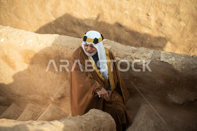 رجل مسن عربي سعودي خليجي يرتدي الزي السعودي الشعبي التقليدي, الزي التراثي للمناسبات الوطنيه, التجول في إحدى المباني الطينيه الشعبيه, بيوت تراثيه قديمه, شعبيات, أحياء أثريه قديمه, جوله بين الأحياء الشعبيه