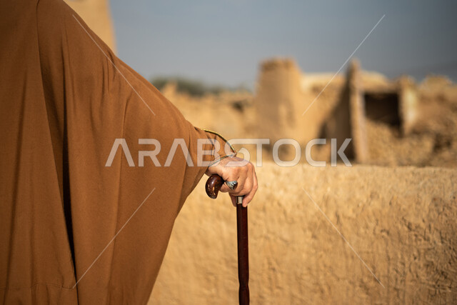 تصوير من الخلف لرجل مسن عربي سعودي خليجي يرتدي الزي السعودي الشعبي التقليدي, الزي التراثي للمناسبات الوطنيه, الوقوف في إحدى المباني الطينيه الشعبيه, رؤيه مستقبليه، المستقبل السعودي، النظر من بعيد, بيوت تراثيه, يوم التأسيس السعودي, مباني أثريه
