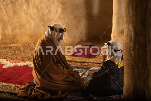 صوره من الخلف لرجل مسن وولد عربيان سعوديان خليجيان يرتديان الزي السعودي الشعبي التقليدي, الصلاه في إحدى المباني الطينيه الشعبيه, بيوت تراثيه قديمه, شعبيات