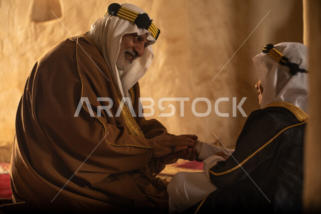 صوره من الخلف لرجل مسن وولد عربيان سعوديان خليجيان يرتديان الزي السعودي الشعبي التقليدي, الصلاه في إحدى المباني الطينيه الشعبيه, بيوت تراثيه قديمه, شعبيات