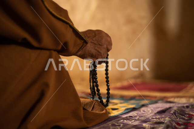 صوره من الخلف لرجل مسن عربي سعودي خليجي يرتدي الزي السعودي الشعبي التقليدي, الصلاه في إحدى المباني الطينيه الشعبيه, بيوت تراثيه قديمه, شعبيات