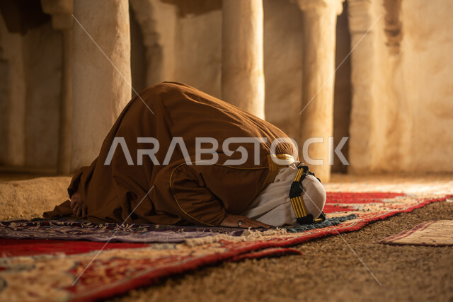 رجل مسن عربي سعودي خليجي يرتدي الزي السعودي الشعبي التقليدي, الصلاه في إحدى المباني الطينيه الشعبيه, بيوت تراثيه قديمه, شعبيات