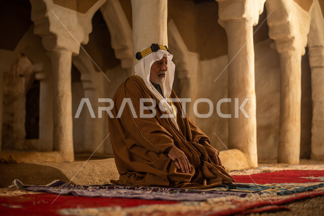 رجل مسن عربي سعودي خليجي يرتدي الزي السعودي الشعبي التقليدي, الصلاه في إحدى المباني الطينيه الشعبيه, بيوت تراثيه قديمه, شعبيات