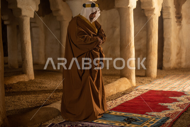 رجل مسن عربي سعودي خليجي يرتدي الزي السعودي الشعبي التقليدي, الصلاه في إحدى المباني الطينيه الشعبيه, بيوت تراثيه قديمه, شعبيات