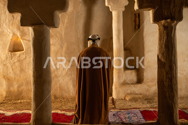 رجل مسن عربي سعودي خليجي يرتدي الزي السعودي الشعبي التقليدي, الصلاه في إحدى المباني الطينيه الشعبيه, بيوت تراثيه قديمه, شعبيات