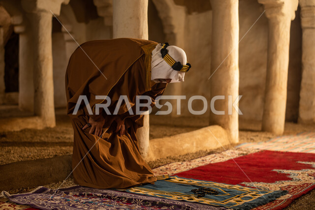 رجل مسن عربي سعودي خليجي يرتدي الزي السعودي الشعبي التقليدي, الصلاه في إحدى المباني الطينيه الشعبيه, بيوت تراثيه قديمه, شعبيات