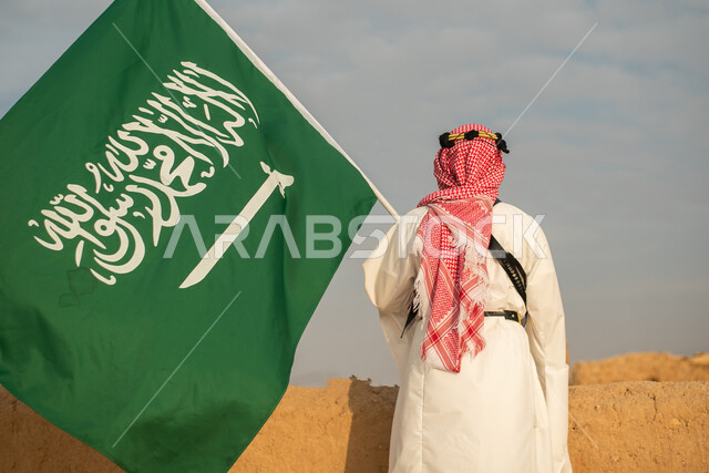 تصوير من الخلف لرجل عربي سعودي خليجي يرتدي الزي السعودي الشعبي التقليدي, الزي التراثي للمناسبات الوطنيه, الوقوف في إحدى المباني الطينيه الشعبيه, رؤيه مستقبليه، المستقبل السعودي، إيماءات النظر من بعيد, بيوت تراثيه قديمه, يوم التأسيس السعودي, مباني أثريه