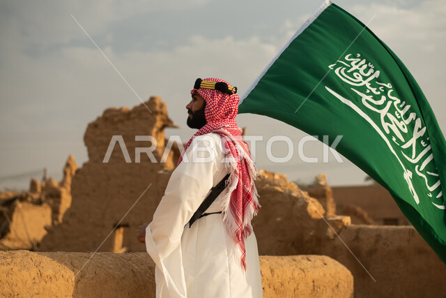 تصوير من الخلف لرجل عربي سعودي خليجي يرتدي الزي السعودي الشعبي التقليدي, الزي التراثي للمناسبات الوطنيه, الوقوف في إحدى المباني الطينيه الشعبيه, رؤيه مستقبليه، المستقبل السعودي، إيماءات النظر من بعيد, بيوت تراثيه قديمه, يوم التأسيس السعودي, مباني أثريه