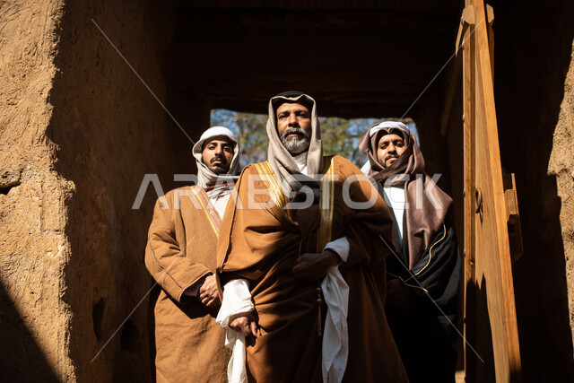 مجموعة من الرجال العرب السعوديون، يوم التأسيس السعودي، تأسيس المملكة 1727م ، أزياء شعبية سعودية، السعودية القديمة، بيوت طينية تراثية قديمة، زي تراثي سعودي للمناسبات الوطنية