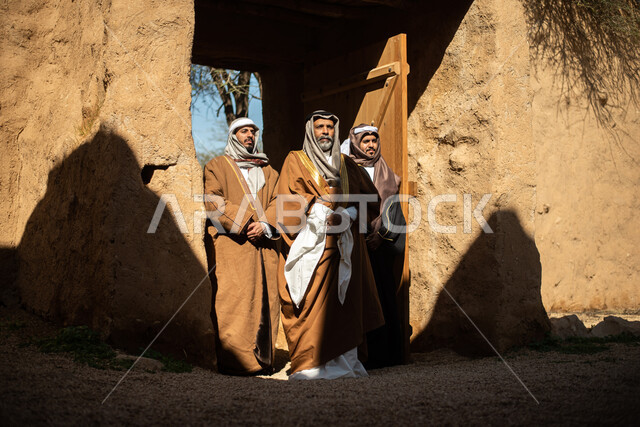مجموعة من الرجال العرب السعوديون، يوم التأسيس السعودي، تأسيس المملكة 1727م ، أزياء شعبية سعودية، السعودية القديمة، بيوت طينية تراثية قديمة، زي تراثي سعودي للمناسبات الوطنية، صورة بالطول الكامل