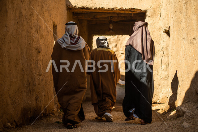 زاوية من الخلف لمجموعة من الرجال العرب السعوديون، يوم التأسيس السعودي، تأسيس المملكة 1727م ، أزياء شعبية سعودية، السعودية القديمة، بيوت طينية تراثية قديمة، زي تراثي سعودي للمناسبات الوطنية، صورة بالطول الكامل