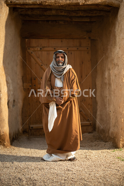 An elderly Saudi Arabian Gulf man, Saudi founding day, the founding of the Kingdom 1727 AD, Saudi folk costumes, old Saudi Arabia, old traditional mud houses, Saudi traditional costume for national occasions, full length photo
